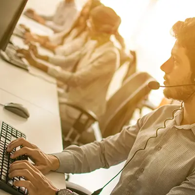 several people in front of computers typing while wearing headsets in an office
