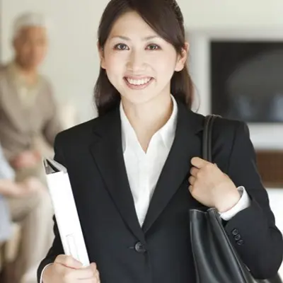 a professionally dressed woman holding a purse and a binder smiling into the camera