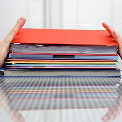 two hands on either side of a red binder filled with papers, pushing in opposite directions