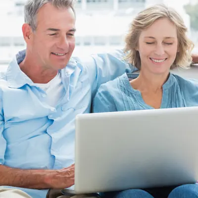 a couple sitting together, smiling and looking at a laptop