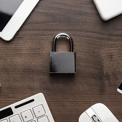 a padlock in the centre of a wooden table with an ipad, a keyboard and a mouse surrounding it