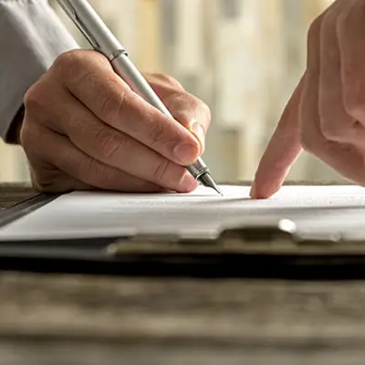 closeup of a finger pointing at a piece of paper and a hand holding a pen signing in place