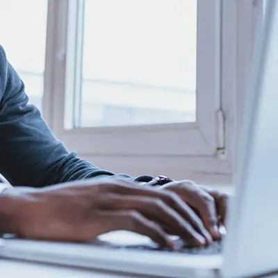 closeup of hands typing on a laptop in front of a window